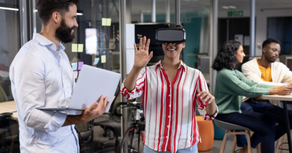 Biracial businesswoman wearing vr headset by caucasian businessman with laptop during meeting. unaltered, business, teamwork, modern office and technology concept.